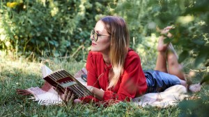 web3-young-blond-woman-wearing-eyeglasses-red-blouse-and-black-skirt-laying-on-the-green-grass-in-the-park-holding-open-book-thinking-pretty-girl-reading-book-in-summer.-student-studying.jpg