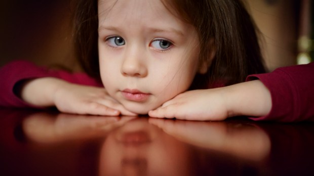 dziewczynka ze smutną miną opiera się na stole
