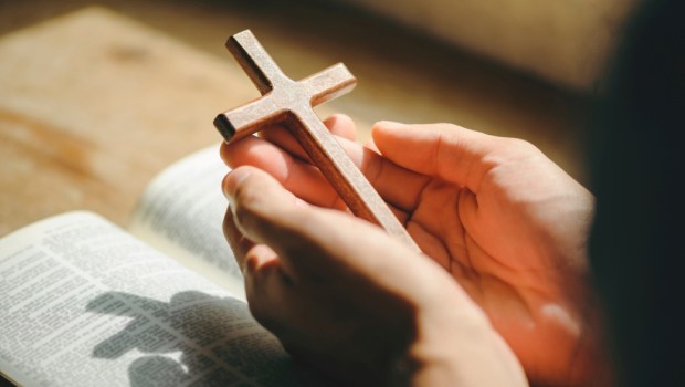 man hands praying to god with the bible and cross