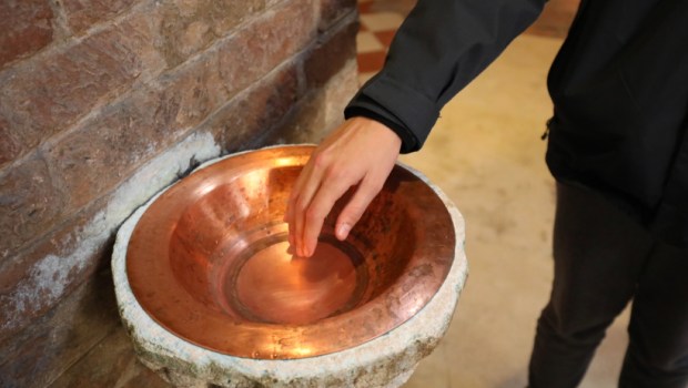 Faithful plunges his hand into the holy water of a Catholic church to make the sign of the cross