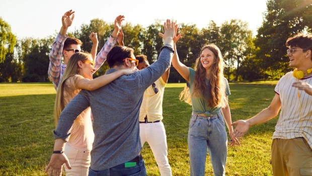 Group of happy young people have fun together while walking in park on warm summer evening