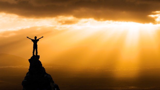 man on the top of a rock meeting sun