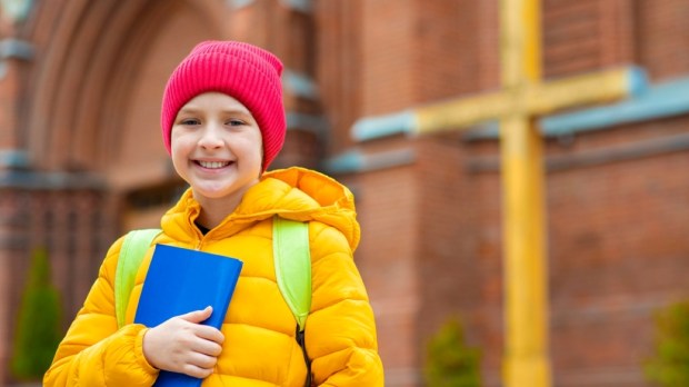 smiling happy child in a hat and jacket, holds a children's bible in his hands, goes to Sunday school