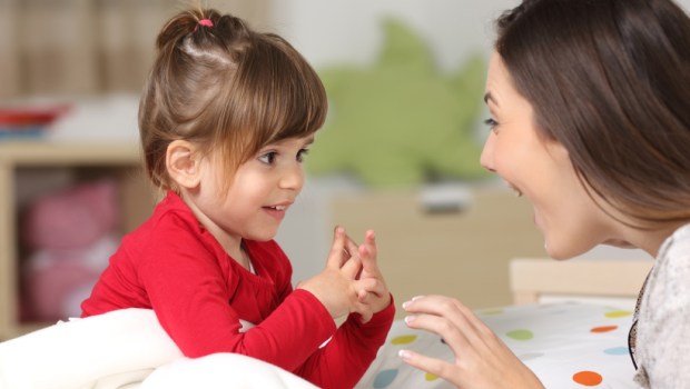 Mother and toddler wearing red shirt playing together on a bed in the bedroom at home