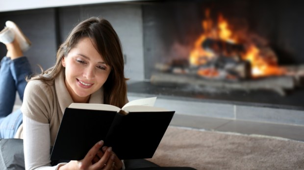 Portrait of beautiful woman reading book by fireplace