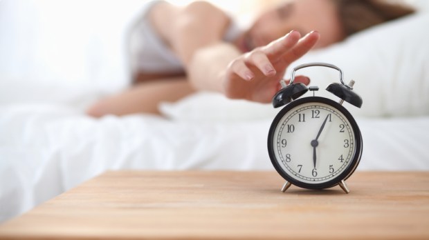 Young sleeping woman and alarm clock in bedroom at home