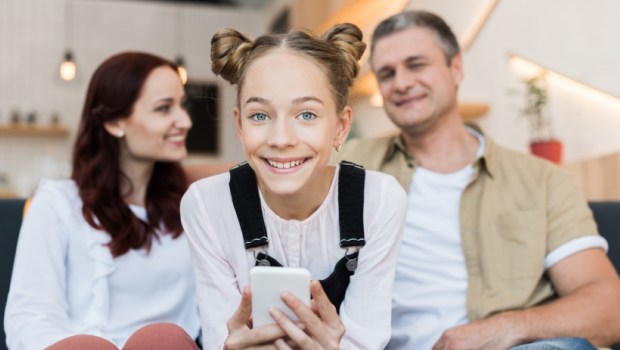 mature parents and teen girl with smartphone in cafe