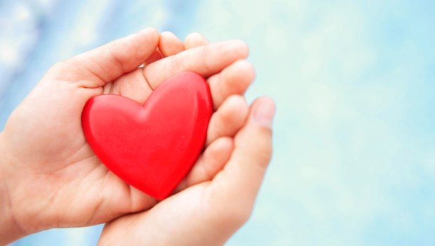 Hands close up holding red heart with blue background