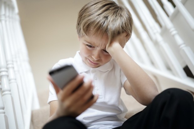 Smutny chłopczyk wpatruje się w telefon