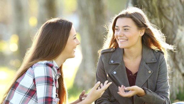 Two friends talking and laughing sitting on the grass in a park