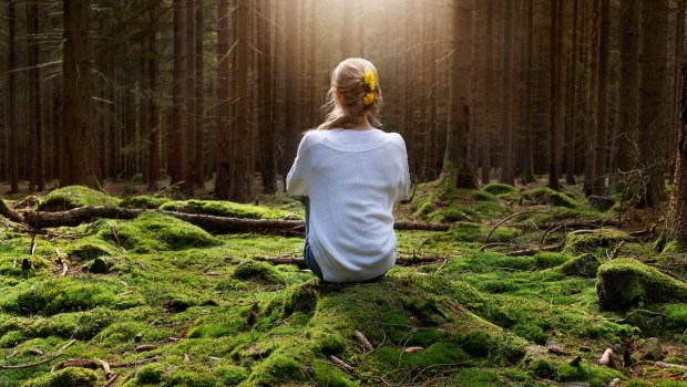 Woman sitting in forest enjoys the silence and beauty of nature
