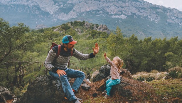Family father and child daughter high five hands traveling in mountains hiking together