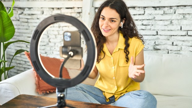 A young Caucasian influencer, creatively recording a vlog on her sofa